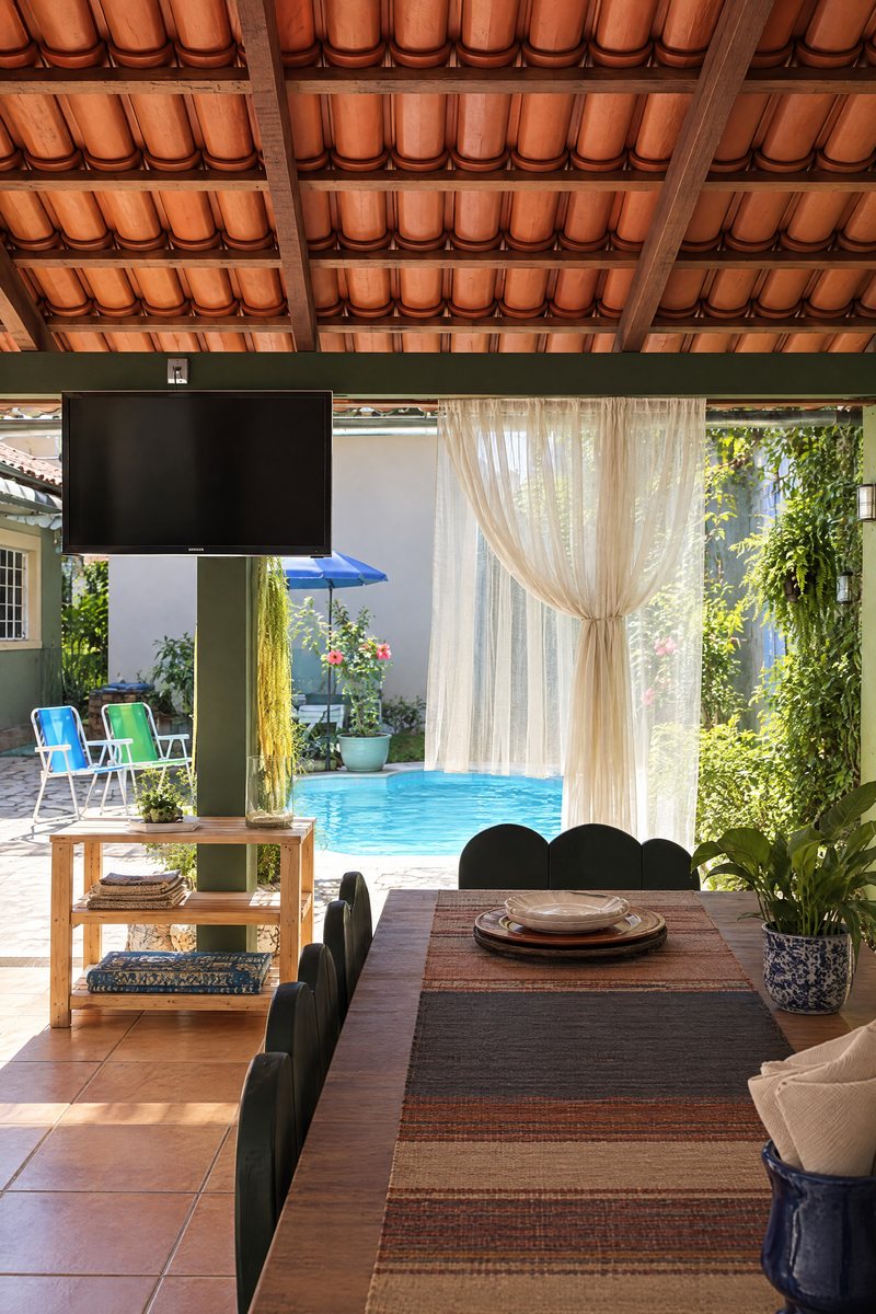 Varanda coberta com televisão, sofá e vista para a piscina